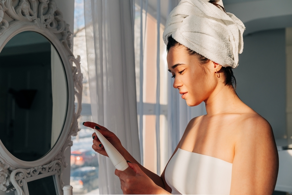 Facial Skincare. Happy Korean asian woman applying Facial serum using dropper standing in modern bathroom. Female moisturizing caring for skin using natural oil looking at the bottle