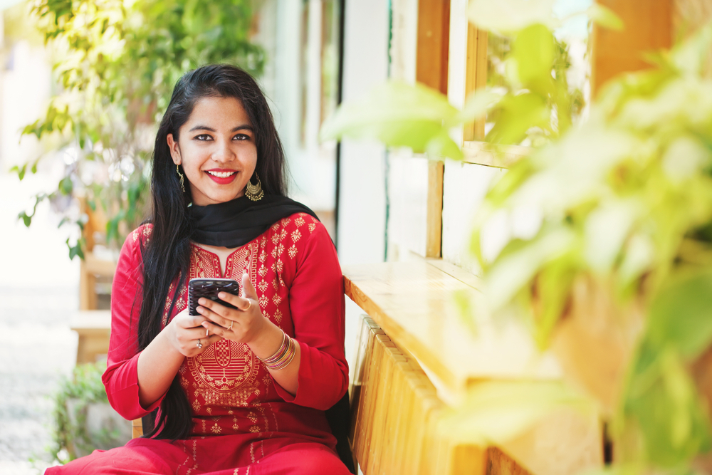 Pretty young indian woman using her phone and looking at camera