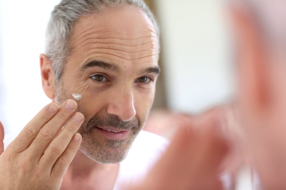 Mature man in front of mirror applying cosmetics