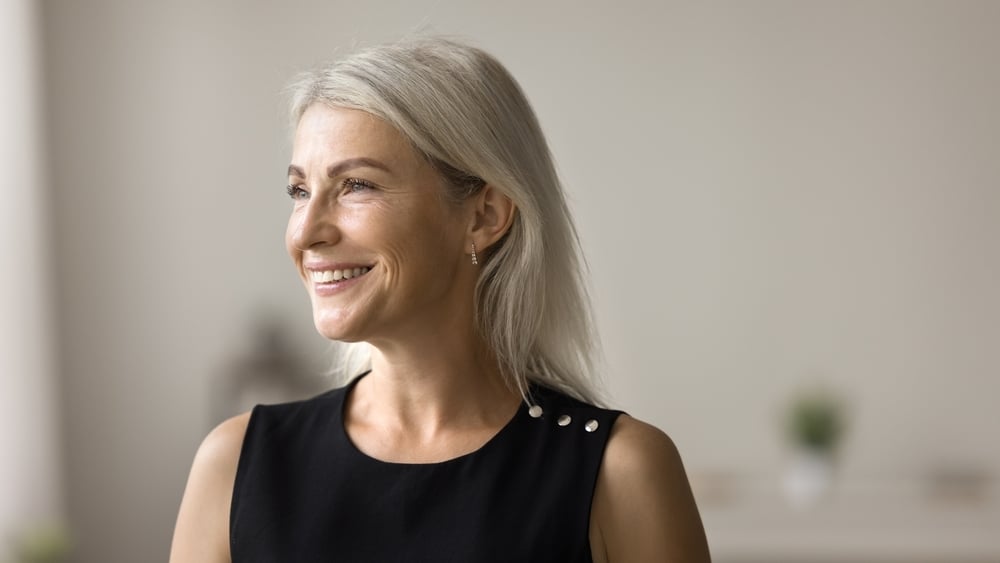 Happy beautiful blonde mature woman banner casual portrait. Cheerful senior lade posing indoors, looking away, thinking on good retirement plans with toothy smile, laughing